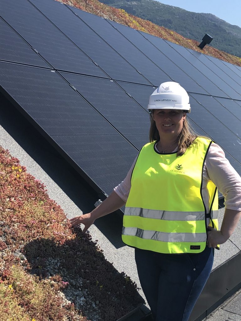 Prosjektsjef Linda Løtvedt Aas foran solceller på taket til næringsbygget skipet i solheimsviken