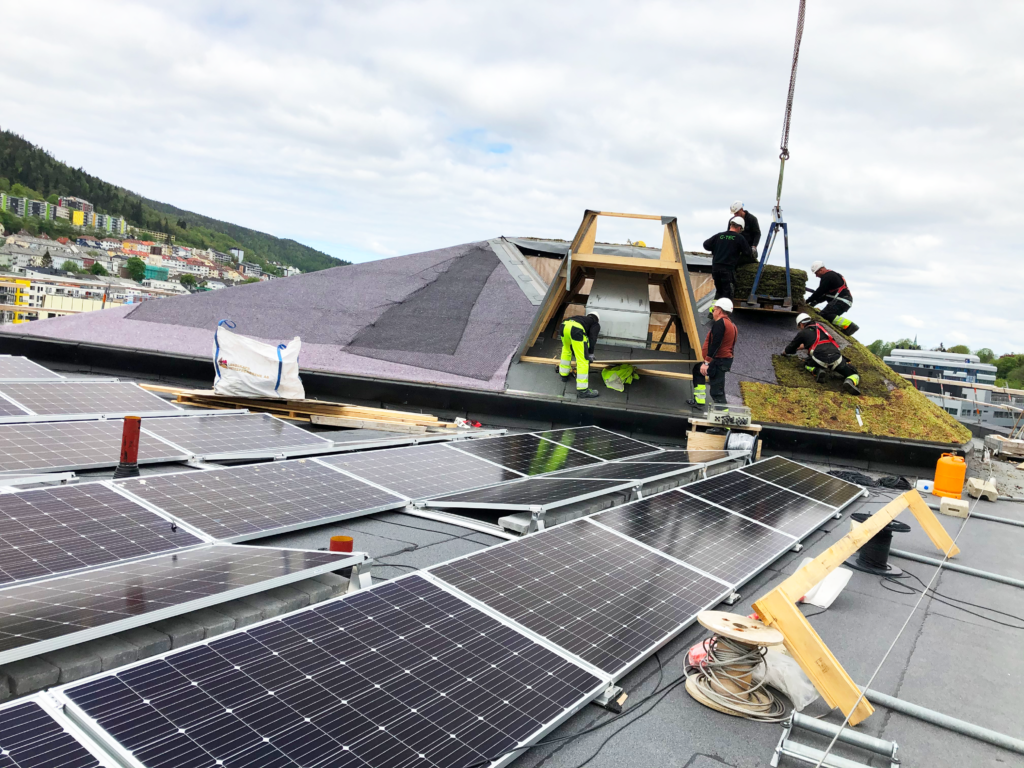 bilde av arbeidere som monterer solceller og grønn vegetasjon på taket til næringsbygget skipet i solheimsviken